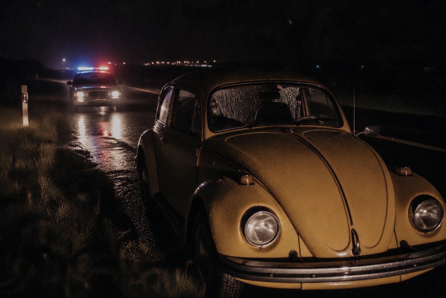 Volkswagen Beetle amarillo detenido en carretera de noche con luces policiales detrás
